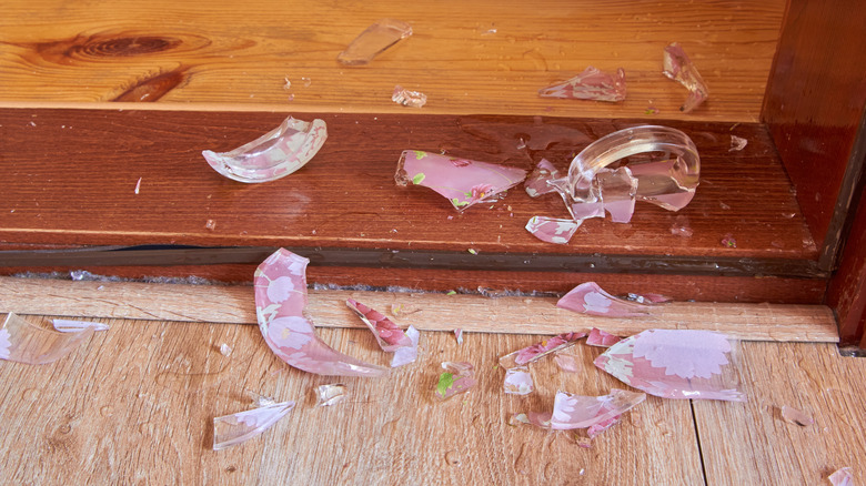 Broken glass pieces from a decorative cup scattered all over a hardwood floor.
