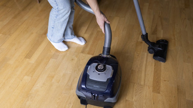 Someone using a vacuum with hose attachment on hardwood floors.