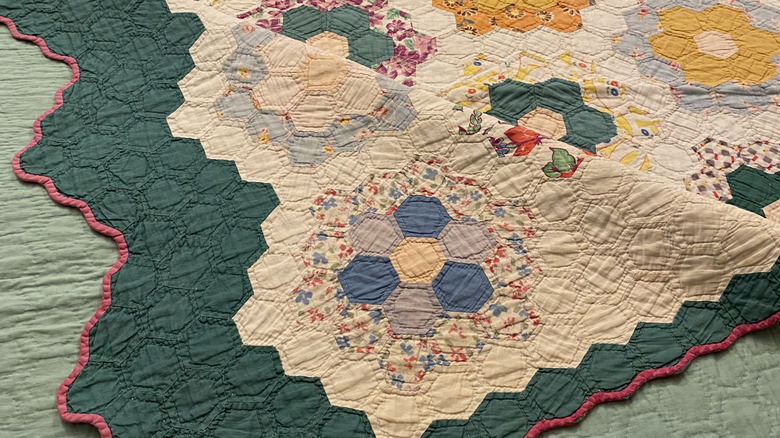 A vintage "grandmother's flowers" quilt (often made from flour sacks) is draped onto a bed