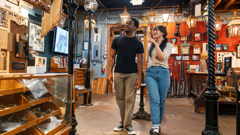 Two people walking through a busy antique shop with hanging lamps