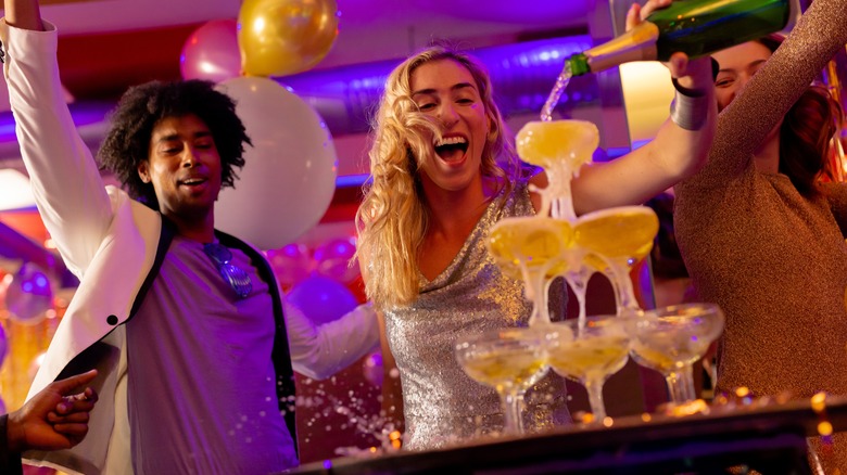 A woman pouring champagne into a coupe tower.