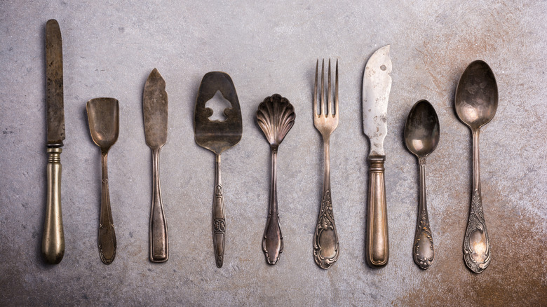Overhead view of collection of tarnished silver-plate utensils on grey background