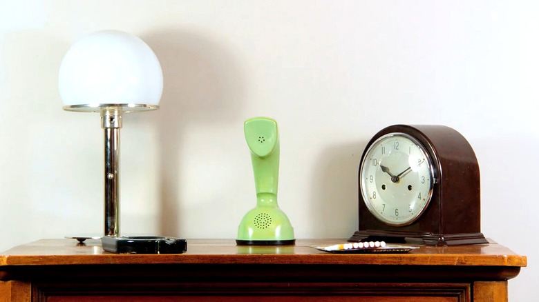 A green Ericofon from the '60s rests atop a dresser next to a lamp and a clock.