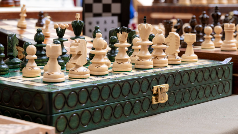 A vintage chess board with an ornate green decorative case surrounded by other vintage chess sets