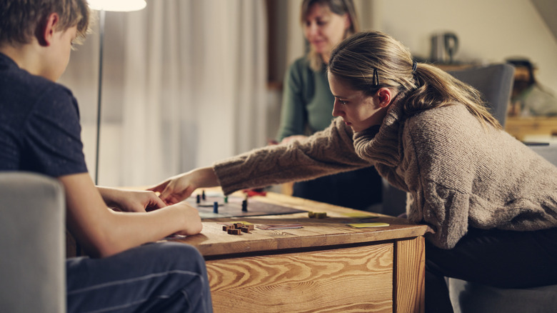 Three people sit around a wooden table and play a board game