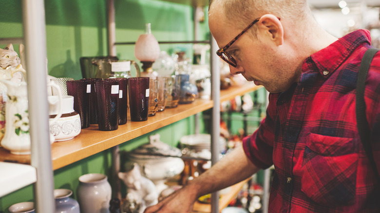 A man reaches down to pick up an item on a shelf at a thrift store.