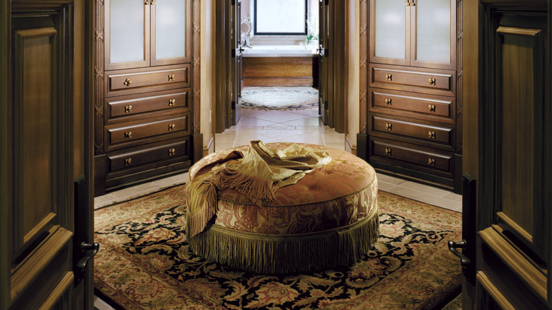 A luxurious walk-in closet space with built-in dark wood wardrobes and a fringed velvet ottoman in the center.