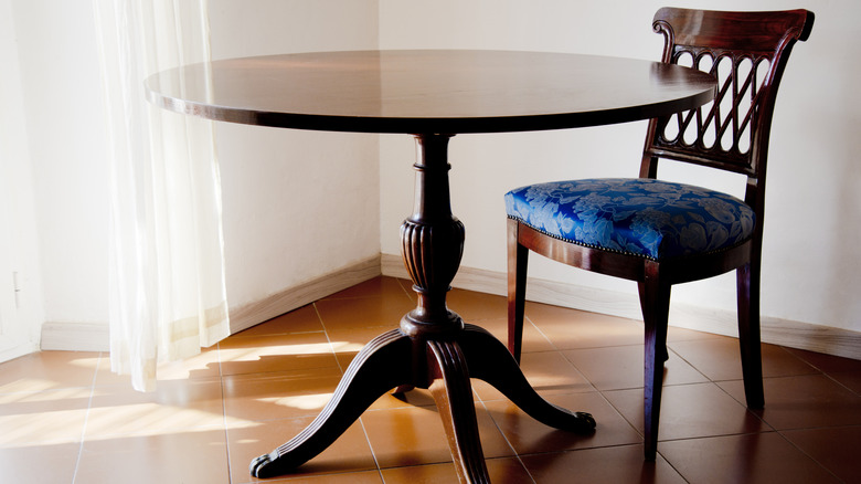 A vintage, dark wood tilt-top table with a matching antique chair.