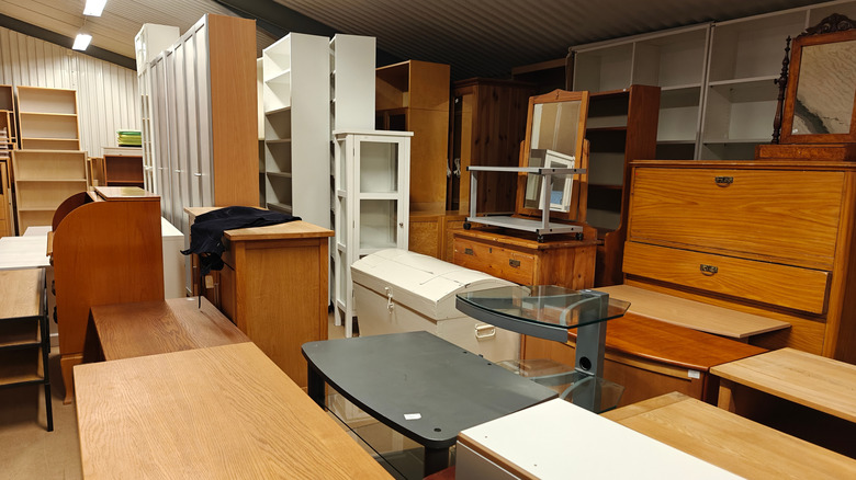 a variety of furniture in a thrift store warehouse including chairs, tables, and shelves