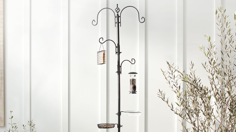 Best Choice Products' bird feeding stations featuring three bird feeders and a shallow bowl hanging from the metal in front of a cream-colored building wall.