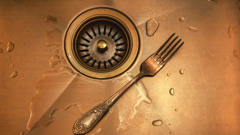 Copper sink with water spots and a fork