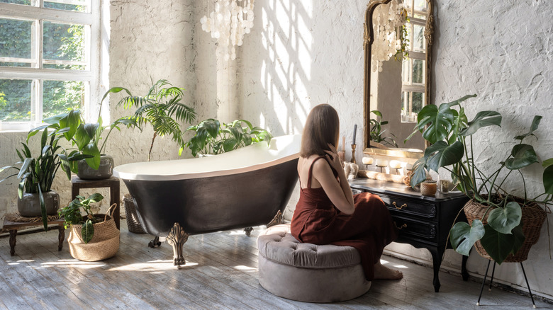 A woman sits in a bright bathroom surrounded by houseplants