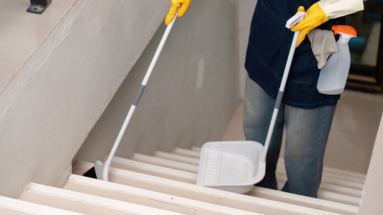 a cleaner wearing apron and gloves sweeping the stairs