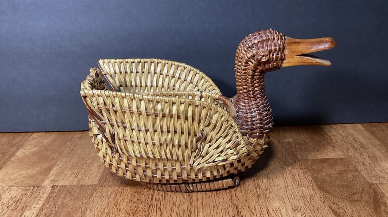 A duck basket made of two colors of rattan on a wood surface with a blue background.