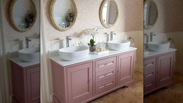 Bathroom with a light pink vanity, floral wallpaper, and gold mirrors