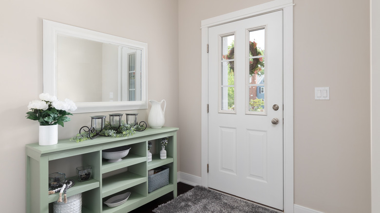 A modern entryway with a mirror and sideboard with decorative items on and in it.