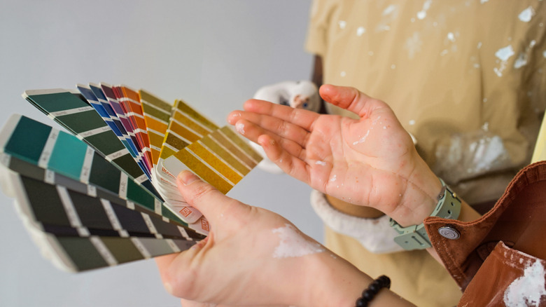A person holding wall color paint swatches while covered in white paint