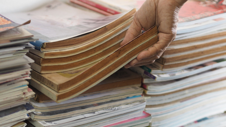 A person picks up vintage magazines from a stack