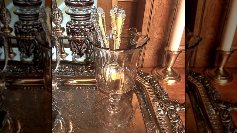 A Victorian spooner in stained brown clear glass holding four silver spoons on a silver tray.