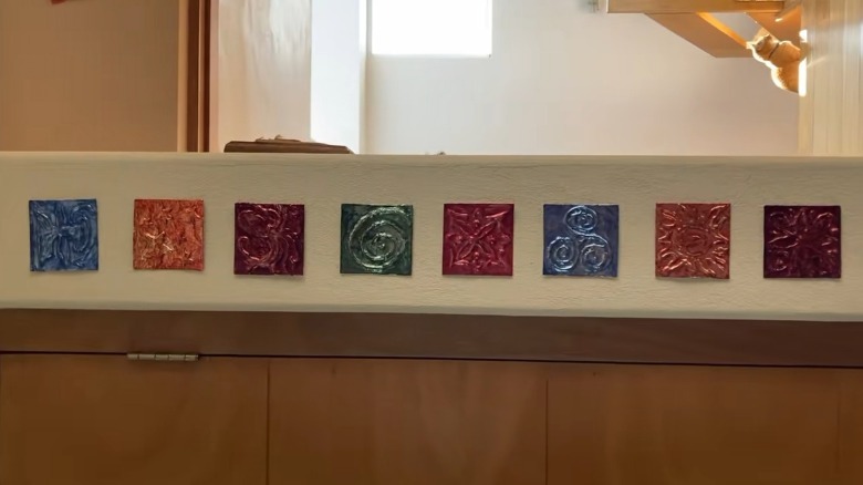 Colorful DIY tin tiles mounted on the wall of a home for display.