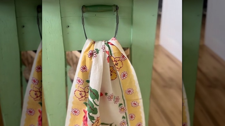 A vintage pastry cutter is used as a towel hanger on the side of a wooden kitchen island.
