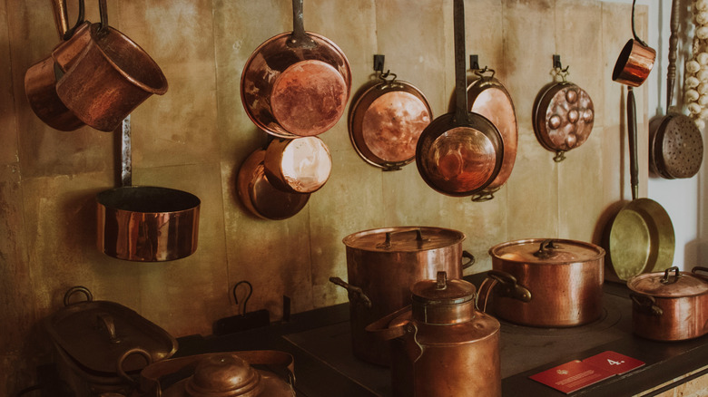 Antique copper pots and pans hanging hanging above a stove.