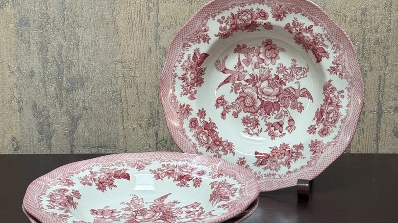 pink floral transferware plates, one on a stand and one on a table