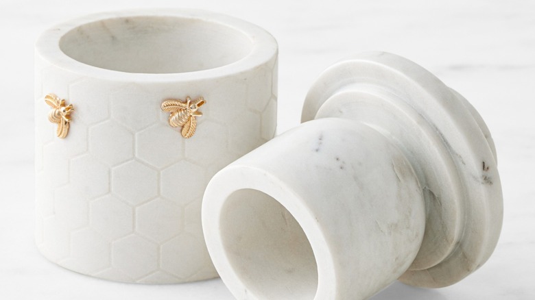 A honeycomb-patterned white marble butter keeper with gold bee accents.
