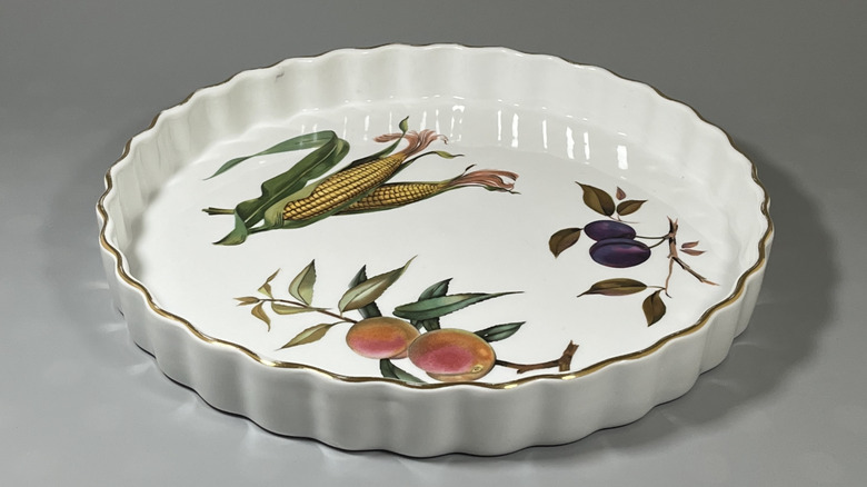 A Royal Worcester Evesham patterned quiche dish is on display with corn, plums, and peaches painted on it.