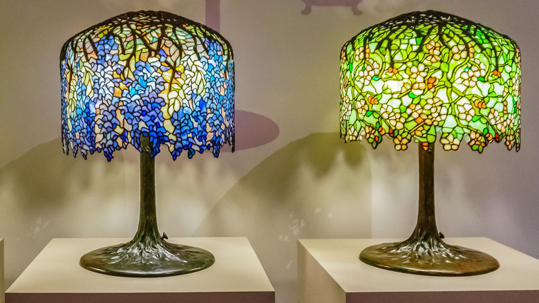 Two Tiffany lamps side by side, one blue and one green, both with elaborate glass floral-patterned lampshades