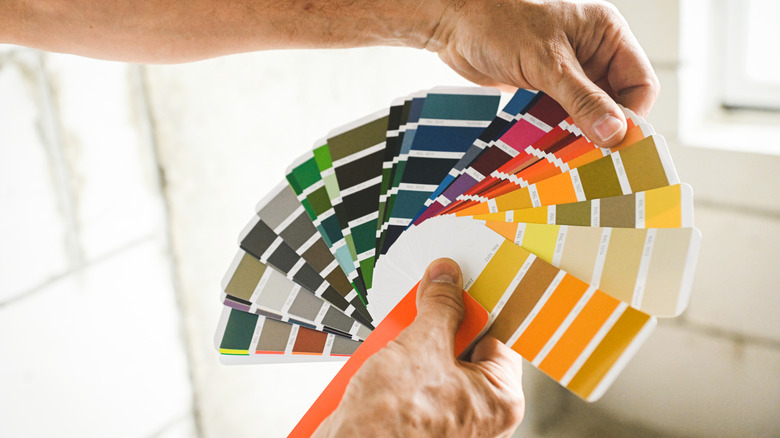 Hands holding a fanned out selection of wall paint swatches in a rainbow of colors