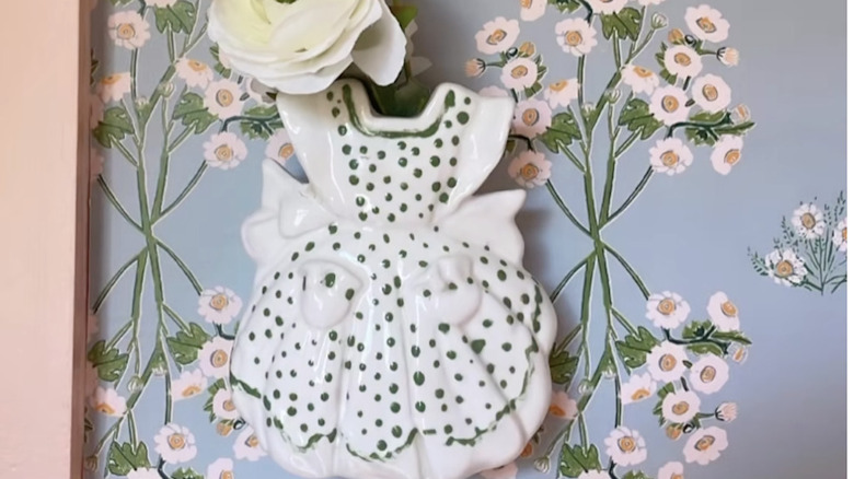 A vintage wall pocket vase styled with a rose and floral wallpaper