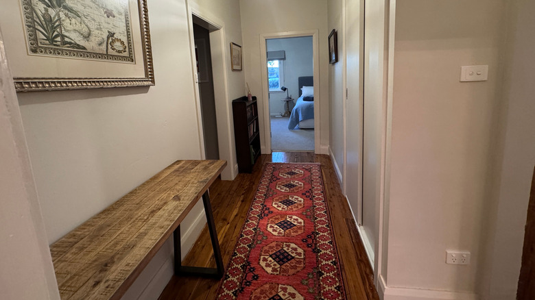 Long black and red Persian rug in hallway with a side table and view into bedroom.