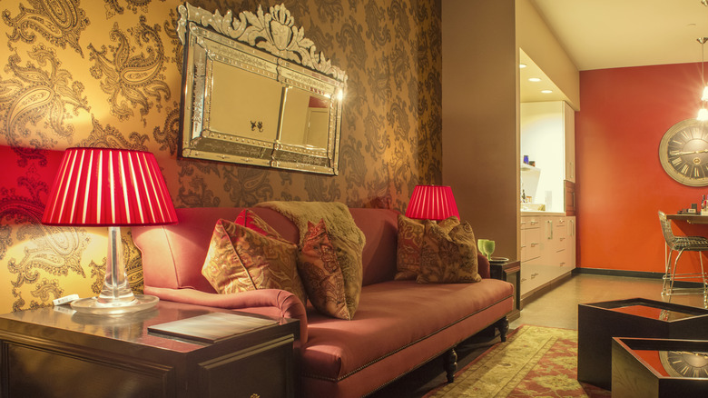 A pink and gold Hollywood Regency-style living room with an ornate gold mirror above a red couch