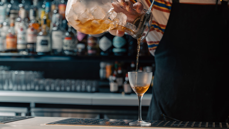 A bartender pours a liquid into a Nick and Nora glass