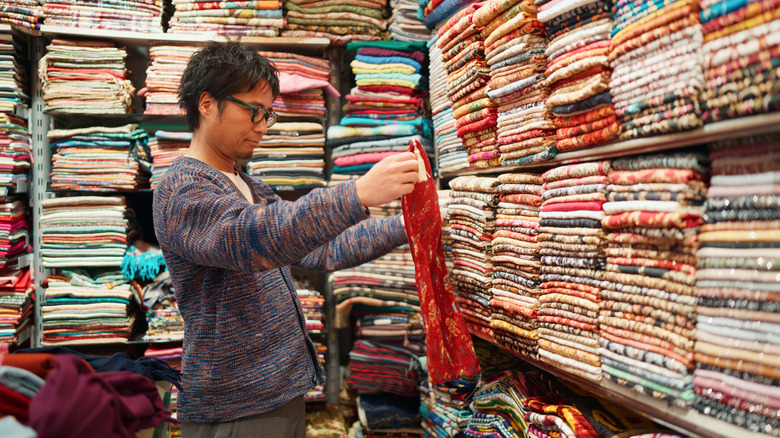 A man looking at clotes and textiles in a store packed with different designs and patterns