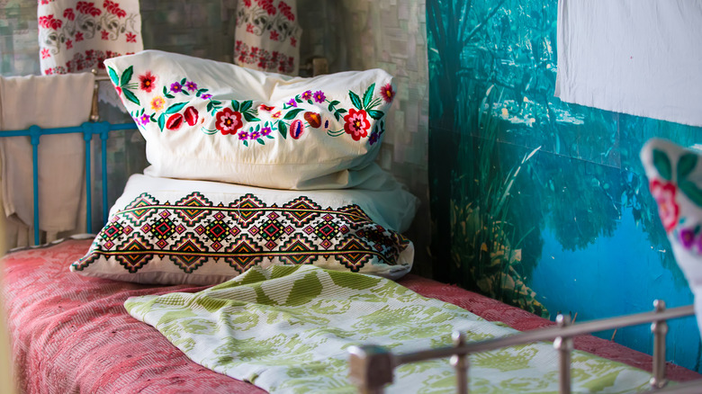 A small bd with various textiles on the pillows and bed, as well as the curtains in the background