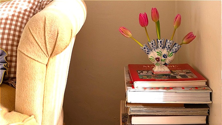 A small porcelain tulipiere on a stack of books holding pink tulips