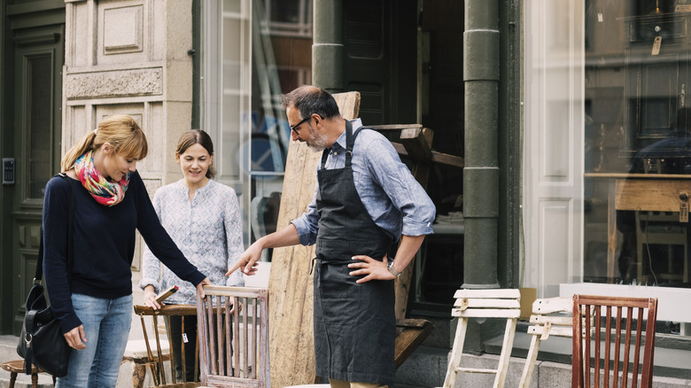 A group of people shop for furniture outside antique store.
