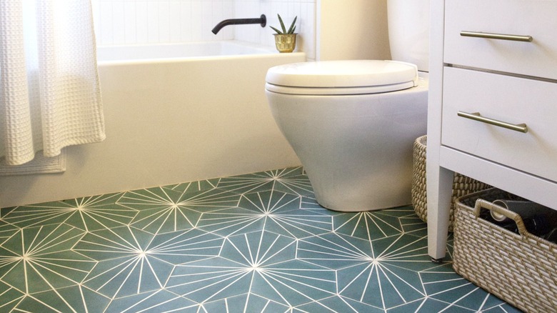 Patterned green vinyl flooring in bathroom with white tub, toilet, and vanity