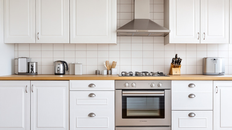 A white kitchen with stainless steel appliances, white cabinets, and light wood floors