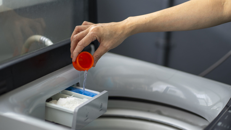 A person is pouring liquid laundry detergent into the dispense drawer