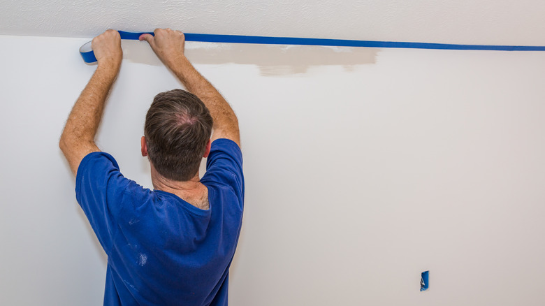 A man puts blue painter's tape between the wall and ceiling.