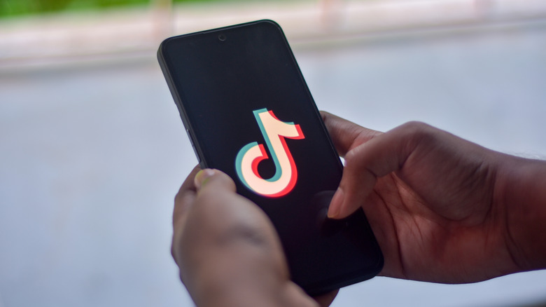 Hands holding a phone with the TikTok logo on the screen