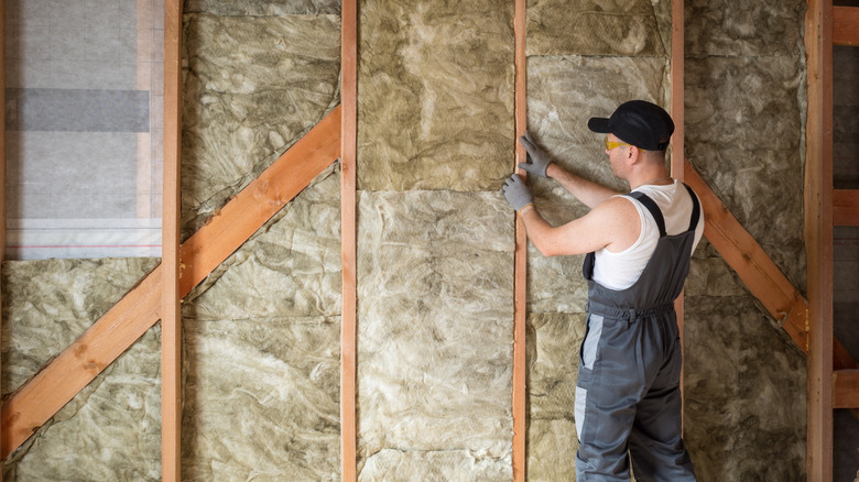 A worker wears gloves while installing fiberglass insulation