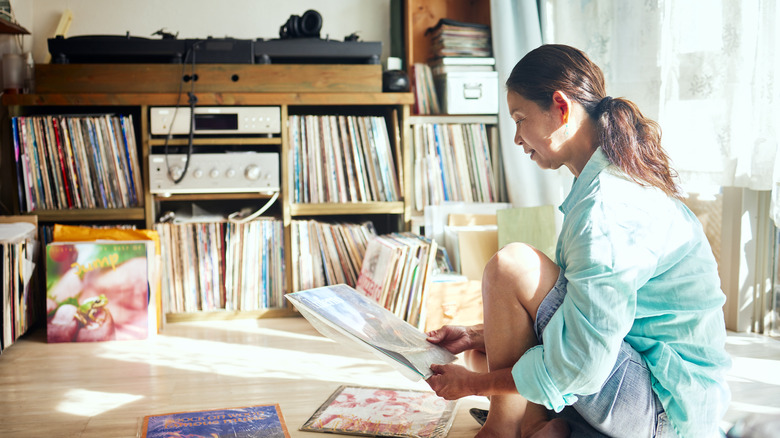 A woman sorting through vinyl records on the floor of a house.