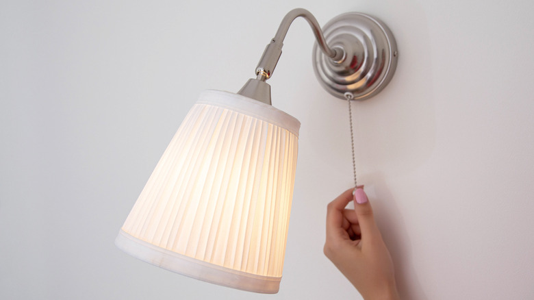 A person turning on a wall sconce