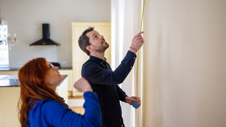 couple measuring blank wall in home