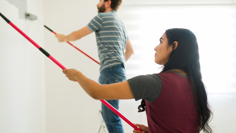 Close up of couple using extension poles to paint their walls