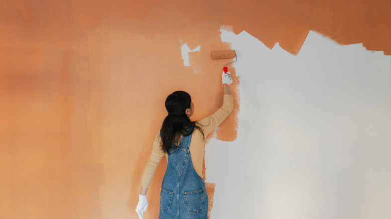 Photo of women painting wall orange using paint roller
